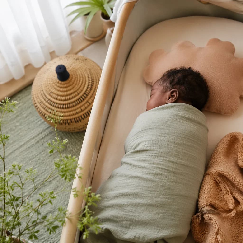 Peaceful swaddled baby in a softly lit pastel nursery with woven accents.