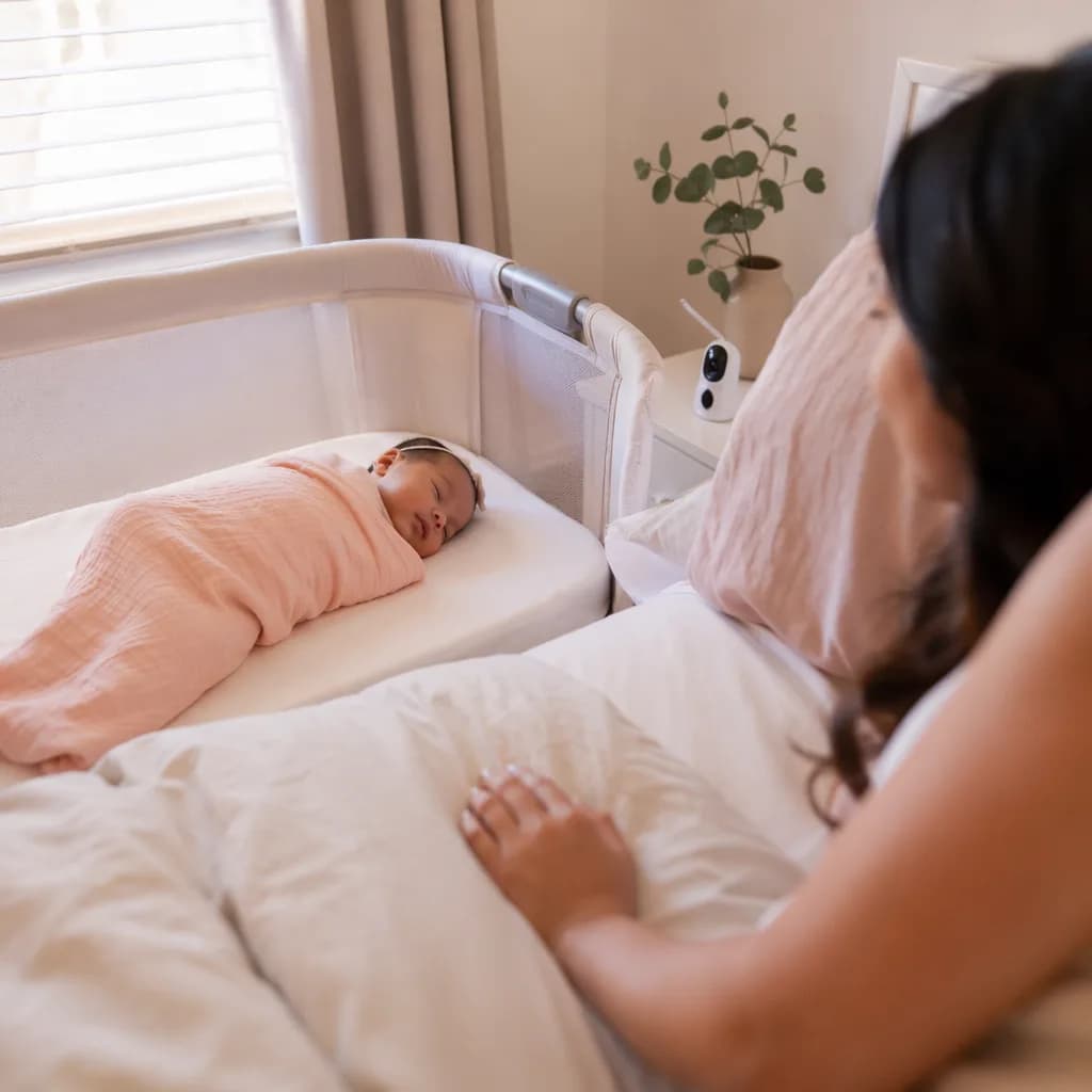 Newborn sleeping peacefully in a bassinet with a parent nearby.